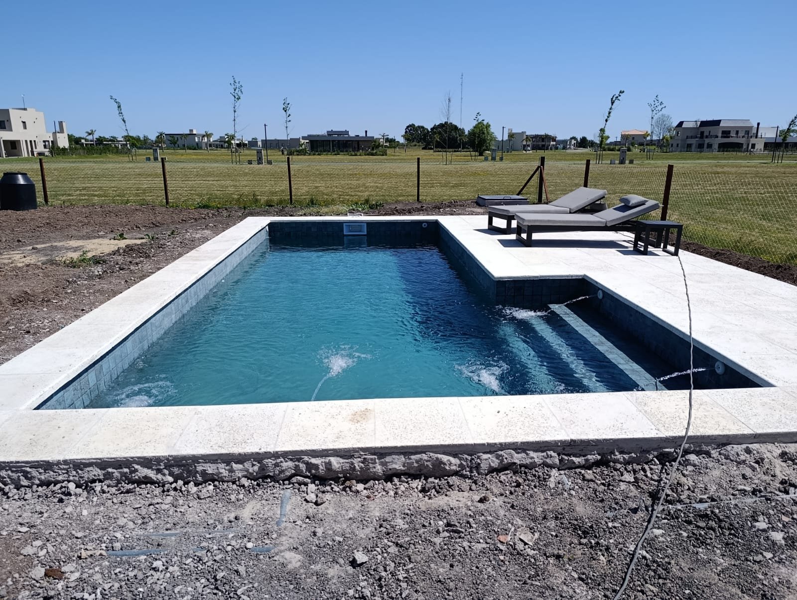 Piscina de hormigón terminada con solárium y reposeras, terminación premium