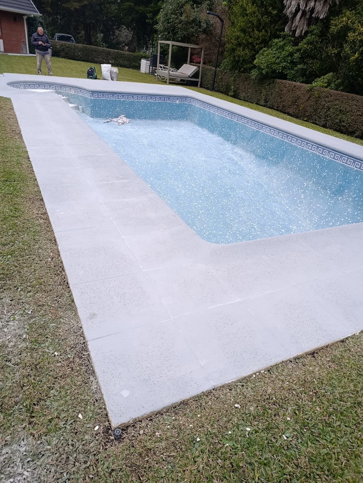 Piscina de hormigón terminada con borde de mosaico greca, en un country