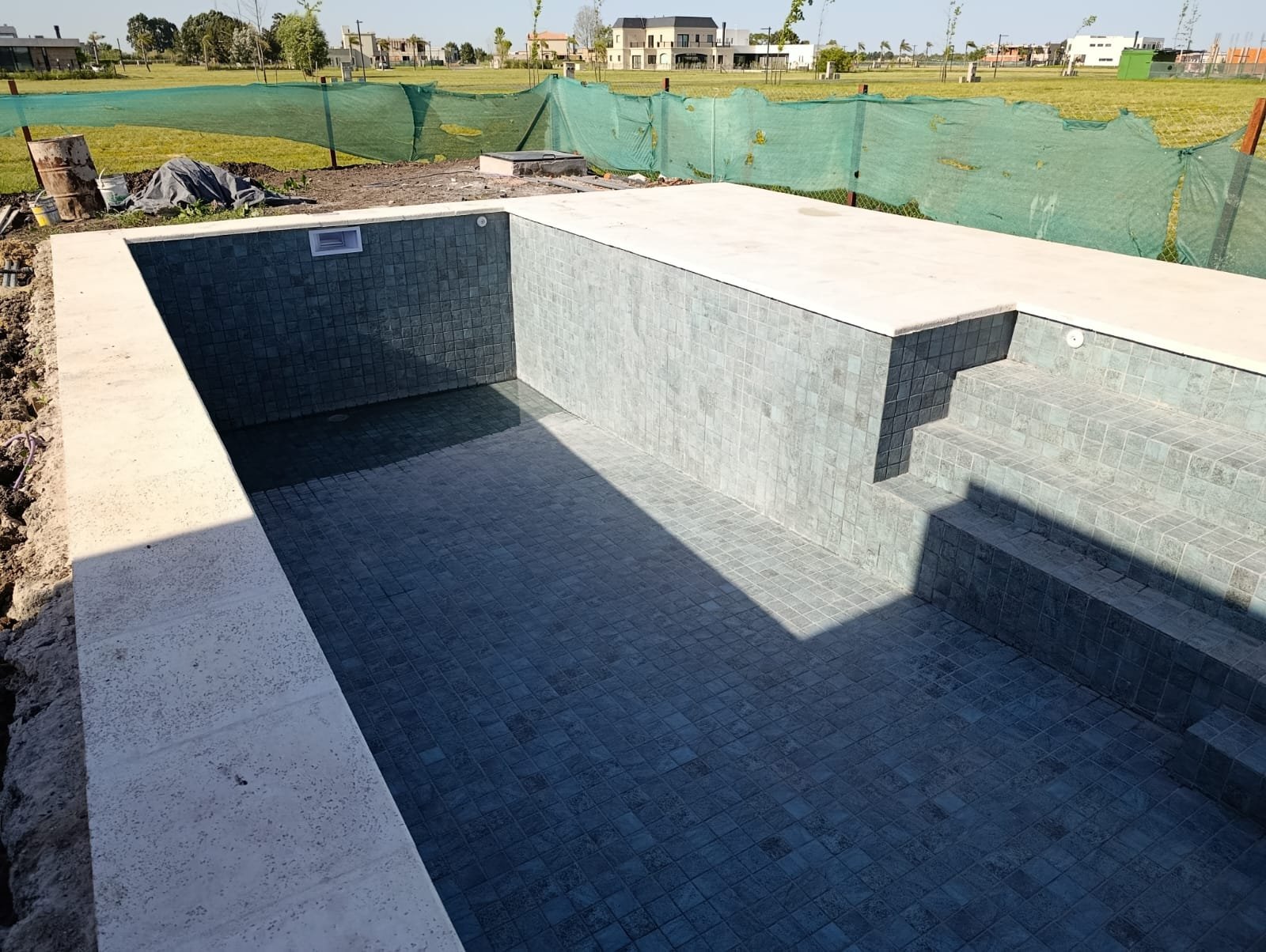 Piscina de hormigón con terminación de mosaico recién finalizada, en un country