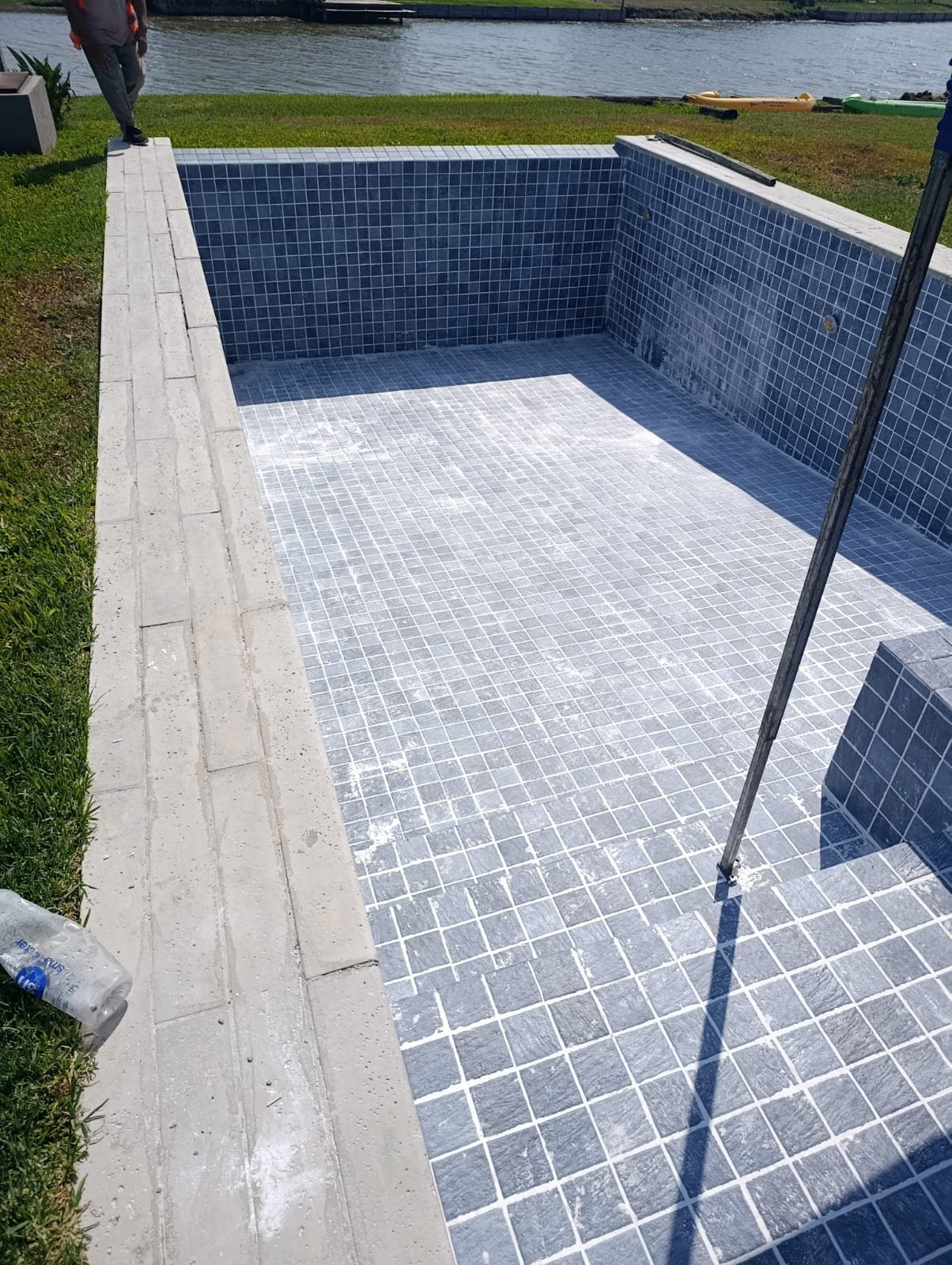 Piscina de hormigón con terminación de mosaico junto a un espejo de agua, en un barrio cerrado